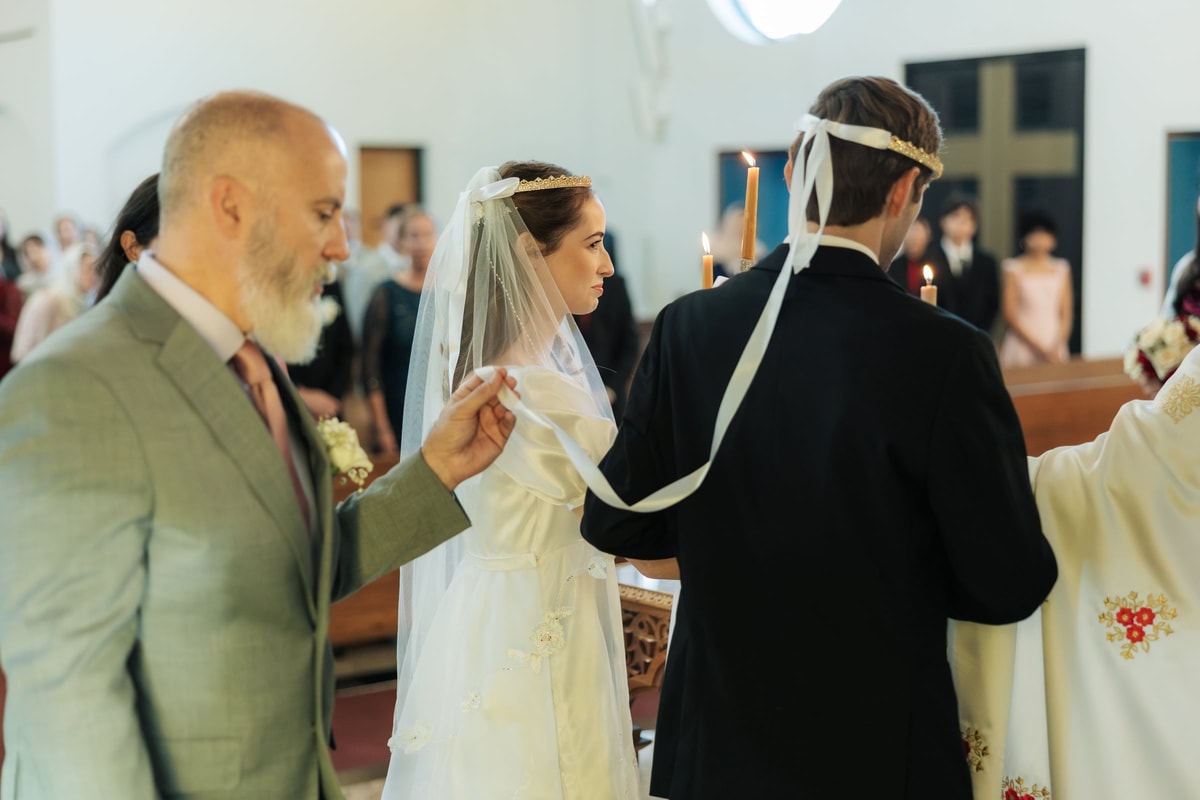 A crowned bride and groom stand with a sponsor during the wedding procession