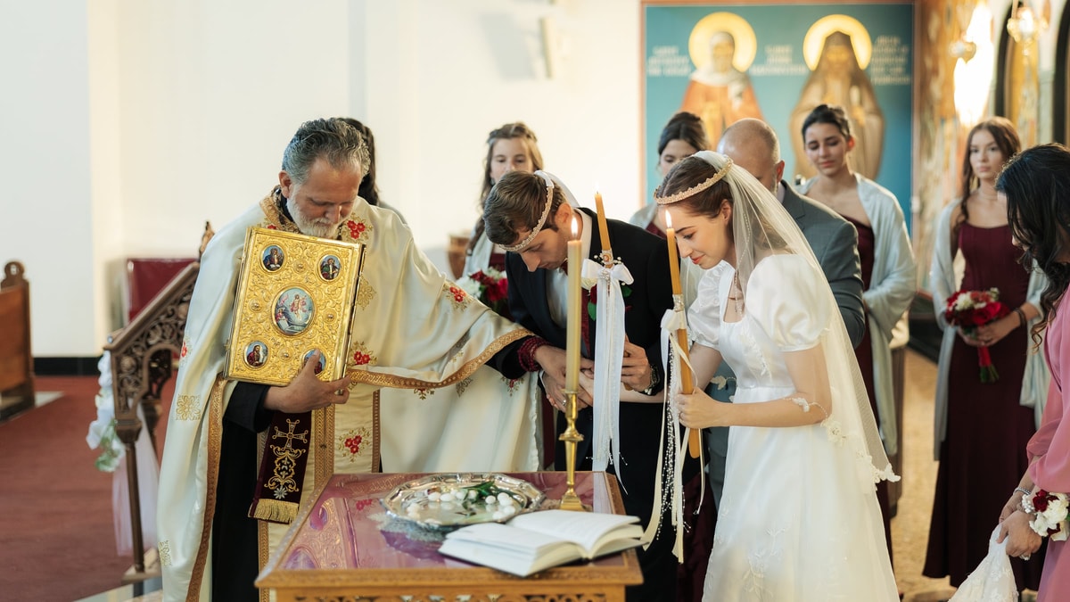 An Orthodox priest carries the Gospel while leading the crowned couple in procession