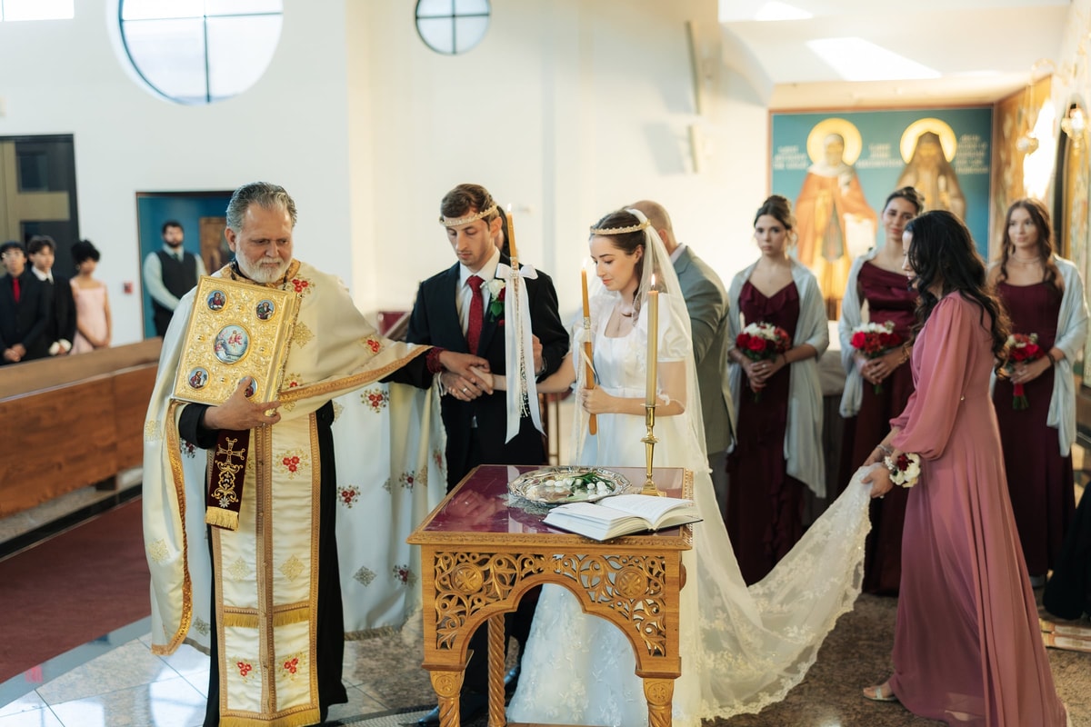 An Orthodox priest carries the Gospel while leading the crowned couple in procession