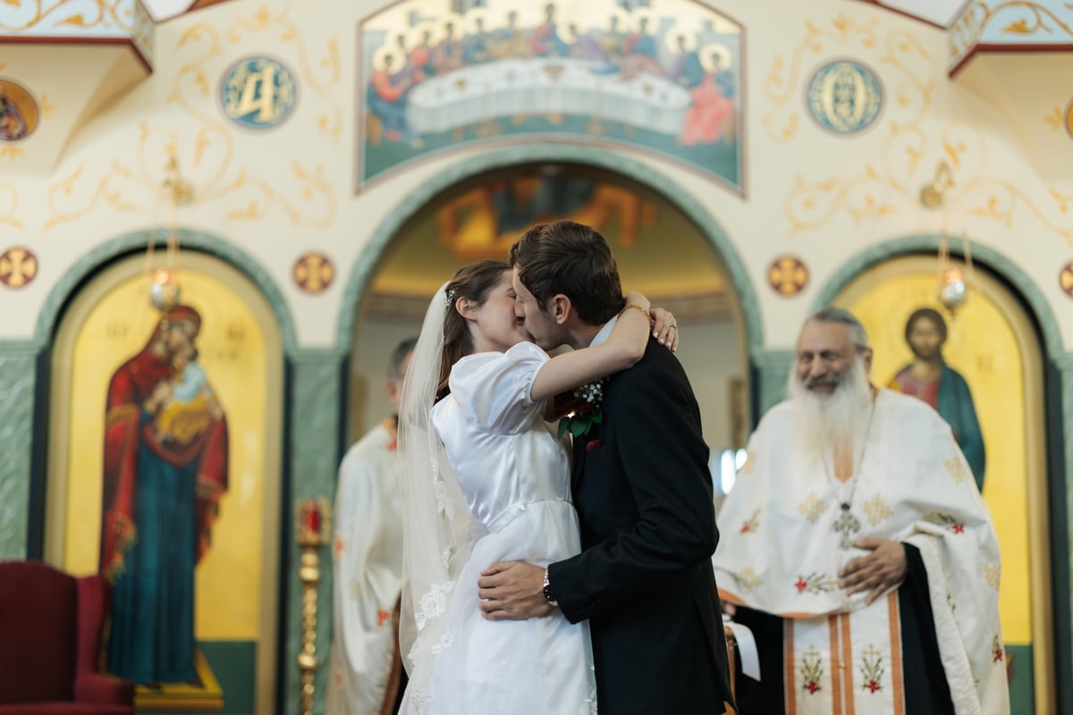 The bride and groom kiss before the iconostasis