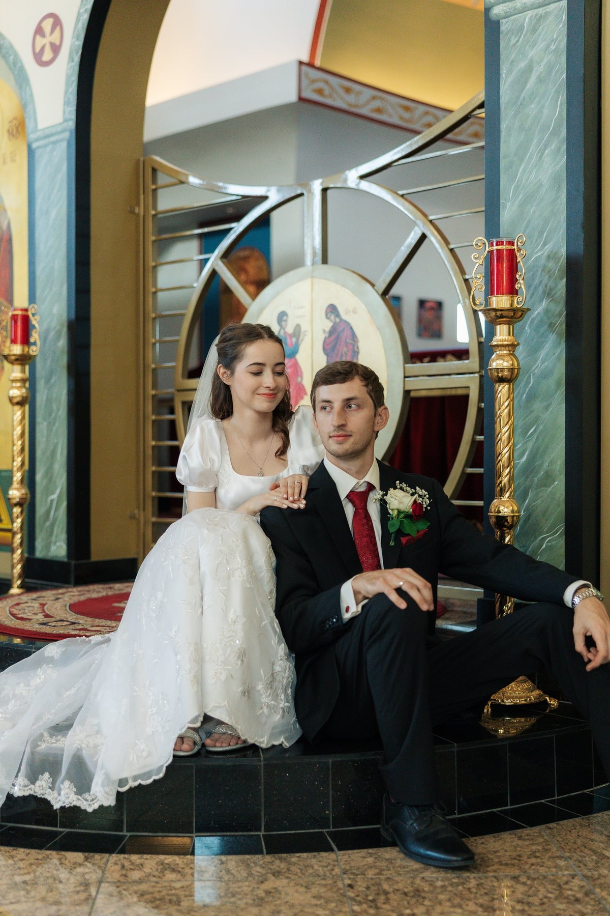 A bride and groom sit together for portraits inside an Orthodox church