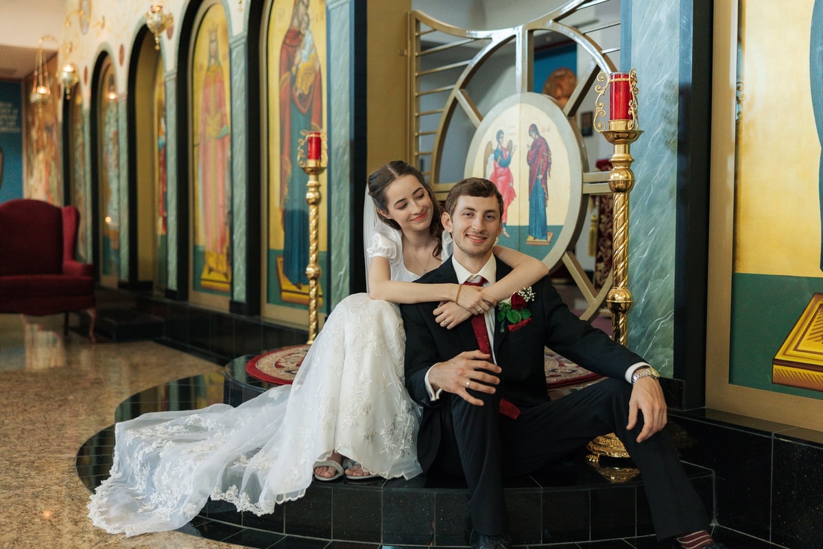 A bride and groom sit together for portraits inside an Orthodox church