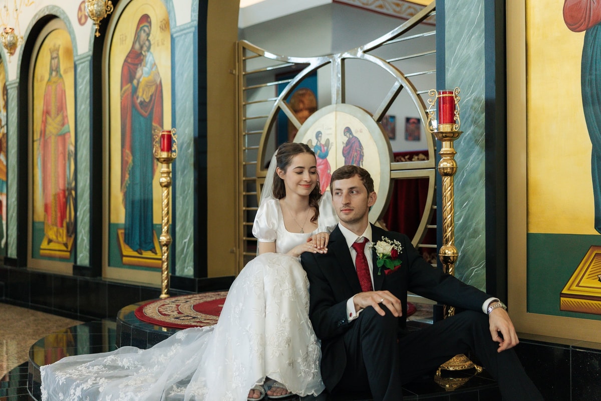 A bride and groom sit together for portraits inside an Orthodox church