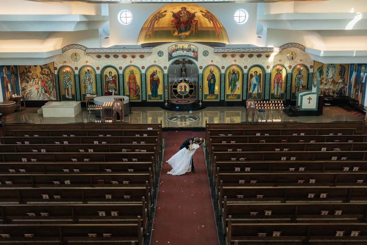 The bride kneels in the center aisle beneath the painted church dome
