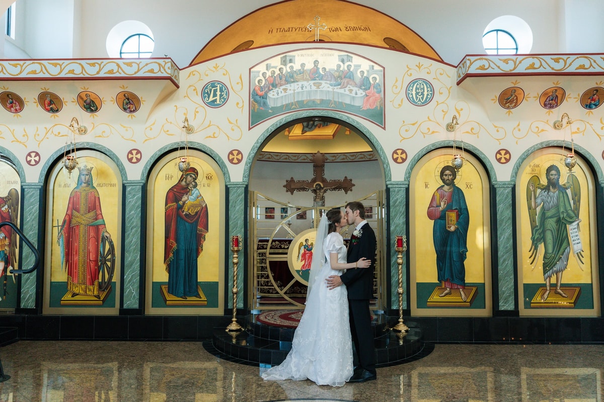 The bride and groom kiss before the iconostasis