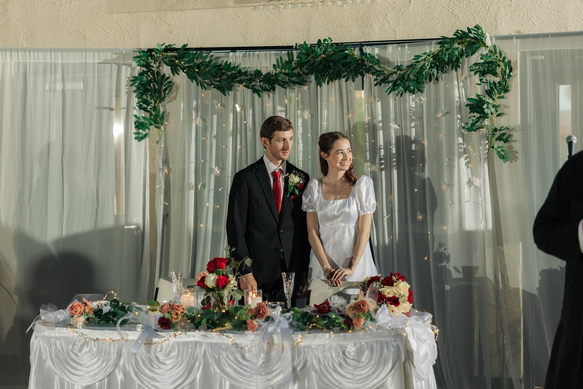 The bride and groom stand behind their decorated reception table