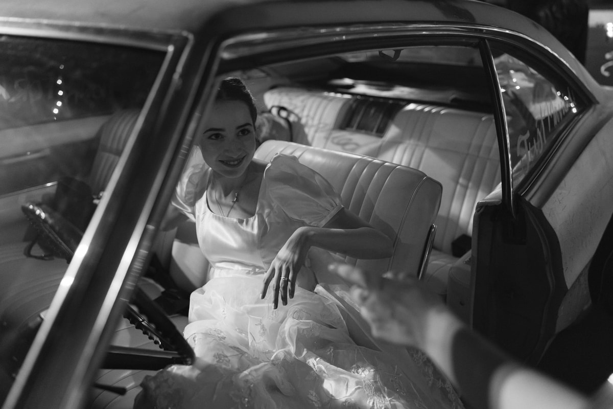 The bride settles into the back seat in a black-and-white photograph